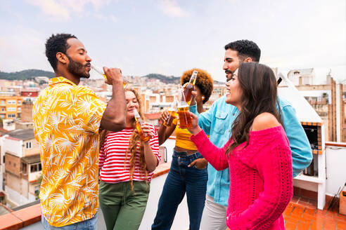 Multiethnische Gruppe von glücklichen jungen Freunden mit Abendessen Grillparty auf dem Dach zu Hause - Multirassische fröhliche junge erwachsene Menschen, die Spaß haben und sich auf einer Terrasse Balkon mit Blick auf die Stadt, Essen und Trinken. - DMDF08631