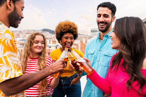 Multiethnische Gruppe von glücklichen jungen Freunden mit Abendessen Grillparty auf dem Dach zu Hause - Multirassische fröhliche junge erwachsene Menschen, die Spaß haben und sich auf einer Terrasse Balkon mit Blick auf die Stadt, Essen und Trinken. - DMDF08643