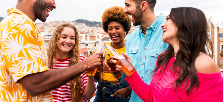 Multiethnische Gruppe von glücklichen jungen Freunden mit Abendessen Grillparty auf dem Dach zu Hause - Multirassische fröhliche junge erwachsene Menschen, die Spaß haben und sich auf einer Terrasse Balkon mit Blick auf die Stadt, Essen und Trinken. - DMDF08644