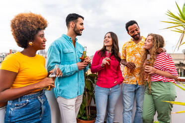 Multiethnische Gruppe von glücklichen jungen Freunden mit Abendessen Grillparty auf dem Dach zu Hause - Multirassische fröhliche junge erwachsene Menschen, die Spaß haben und sich auf einer Terrasse Balkon mit Blick auf die Stadt, Essen und Trinken. - DMDF08649