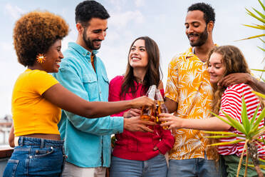 Multiethnische Gruppe von glücklichen jungen Freunden mit Abendessen Grillparty auf dem Dach zu Hause - Multirassische fröhliche junge erwachsene Menschen, die Spaß haben und sich auf einer Terrasse Balkon mit Blick auf die Stadt, Essen und Trinken. - DMDF08654