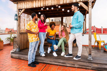 Multiethnische Gruppe von glücklichen jungen Freunden mit Abendessen Grillparty auf dem Dach zu Hause - Multirassische fröhliche junge erwachsene Menschen, die Spaß haben und sich auf einer Terrasse Balkon mit Blick auf die Stadt, Essen und Trinken. - DMDF08656