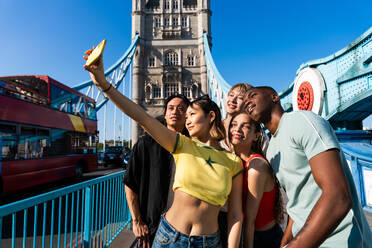 Multirassische Gruppe von glücklichen jungen Freunden in der Londoner City - Multiethnische Teenager treffen sich und haben Spaß in der Tower Bridge, UK - Konzepte über jugendlichen Lebensstil, Reisen und Tourismus - DMDF08665