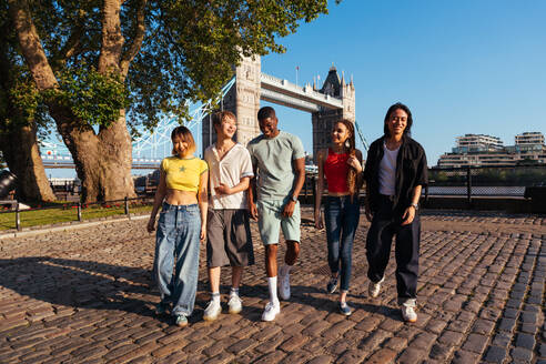 Multirassische Gruppe von glücklichen jungen Freunden in der Londoner City - Multiethnische Teenager treffen sich und haben Spaß in der Tower Bridge, UK - Konzepte über jugendlichen Lebensstil, Reisen und Tourismus - DMDF08689