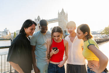 Multirassische Gruppe von glücklichen jungen Freunden in der Londoner City - Multiethnische Teenager treffen sich und haben Spaß in der Tower Bridge, UK - Konzepte über jugendlichen Lebensstil, Reisen und Tourismus - DMDF08695