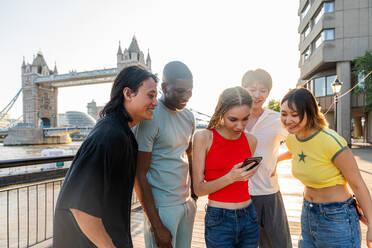 Multirassische Gruppe von glücklichen jungen Freunden in der Londoner City - Multiethnische Teenager treffen sich und haben Spaß in der Tower Bridge, UK - Konzepte über jugendlichen Lebensstil, Reisen und Tourismus - DMDF08696