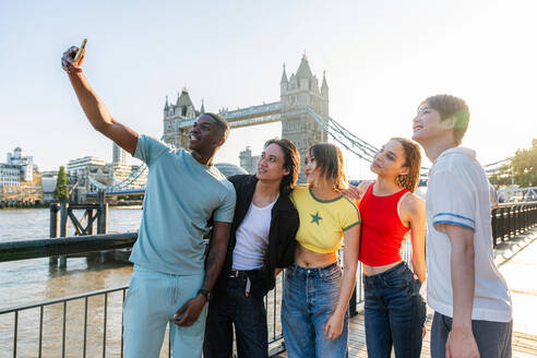 Multirassische Gruppe von glücklichen jungen Freunden in der Londoner City - Multiethnische Teenager treffen sich und haben Spaß in der Tower Bridge, UK - Konzepte über jugendlichen Lebensstil, Reisen und Tourismus - DMDF08700