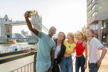 Multirassische Gruppe von glücklichen jungen Freunden in der Londoner City - Multiethnische Teenager treffen sich und haben Spaß in der Tower Bridge, UK - Konzepte über jugendlichen Lebensstil, Reisen und Tourismus - DMDF08701