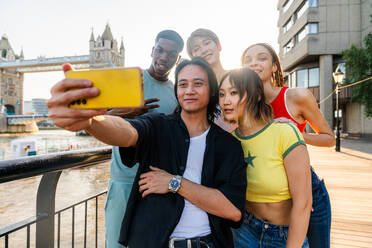 Multirassische Gruppe von glücklichen jungen Freunden in der Londoner City - Multiethnische Teenager treffen sich und haben Spaß in der Tower Bridge, UK - Konzepte über jugendlichen Lebensstil, Reisen und Tourismus - DMDF08706