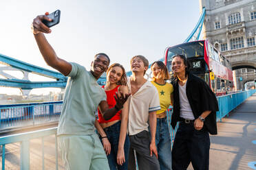 Multirassische Gruppe von glücklichen jungen Freunden in der Londoner City - Multiethnische Teenager treffen sich und haben Spaß in der Tower Bridge, UK - Konzepte über jugendlichen Lebensstil, Reisen und Tourismus - DMDF08722