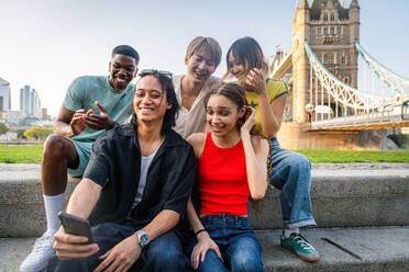 Multirassische Gruppe von glücklichen jungen Freunden in der Londoner City - Multiethnische Teenager treffen sich und haben Spaß in der Tower Bridge, UK - Konzepte über jugendlichen Lebensstil, Reisen und Tourismus - DMDF08723