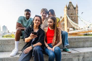 Multirassische Gruppe von glücklichen jungen Freunden in der Londoner City - Multiethnische Teenager treffen sich und haben Spaß in der Tower Bridge, UK - Konzepte über jugendlichen Lebensstil, Reisen und Tourismus - DMDF08724