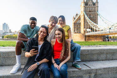 Multirassische Gruppe von glücklichen jungen Freunden in der Londoner City - Multiethnische Teenager treffen sich und haben Spaß in der Tower Bridge, UK - Konzepte über jugendlichen Lebensstil, Reisen und Tourismus - DMDF08725