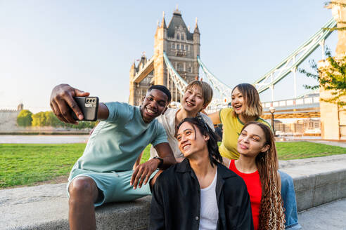 Multirassische Gruppe von glücklichen jungen Freunden in der Londoner City - Multiethnische Teenager treffen sich und haben Spaß in der Tower Bridge, UK - Konzepte über jugendlichen Lebensstil, Reisen und Tourismus - DMDF08727