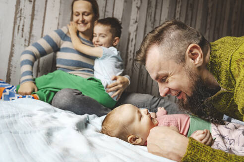 Glücklicher Vater umarmt Baby Tochter und Mutter sitzt mit Sohn auf dem Bett zu Hause - IHF01854