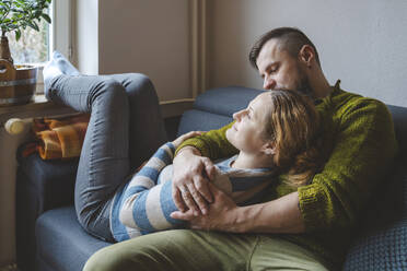 Mann umarmt Frau auf Sofa zu Hause - IHF01864