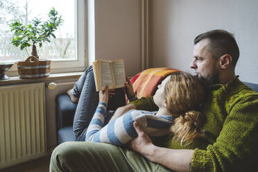 Frau liegt auf dem Schoß eines Mannes und liest ein Buch zu Hause - IHF01865