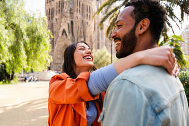 Multiracial beautiful happy couple of lovers dating at Sagrada Familia, Barcelona - Multiethnic tourists travelling in Europe and visiting a city in Spain, concepts about tourism and people lifestyle - DMDF08746