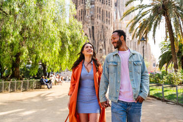 Multiracial beautiful happy couple of lovers dating at Sagrada Familia, Barcelona - Multiethnic tourists travelling in Europe and visiting a city in Spain, concepts about tourism and people lifestyle - DMDF08749