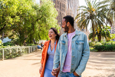 Multiracial beautiful happy couple of lovers dating at Sagrada Familia, Barcelona - Multiethnic tourists travelling in Europe and visiting a city in Spain, concepts about tourism and people lifestyle - DMDF08751