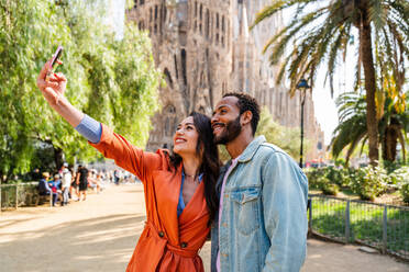 Multiracial beautiful happy couple of lovers dating at Sagrada Familia, Barcelona - Multiethnic tourists travelling in Europe and visiting a city in Spain, concepts about tourism and people lifestyle - DMDF08754