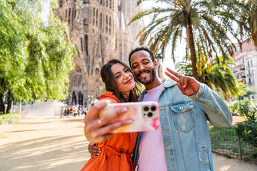 Multiracial beautiful happy couple of lovers dating at Sagrada Familia, Barcelona - Multiethnic tourists travelling in Europe and visiting a city in Spain, concepts about tourism and people lifestyle - DMDF08756