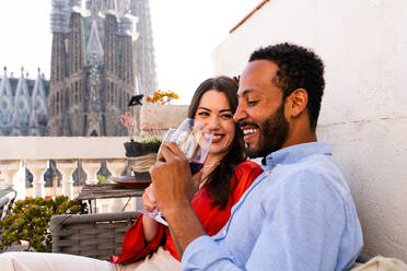 Multiracial beautiful happy couple of lovers dating on rooftop balcony at Sagrada Familia, Barcelona - Multiethnic people having romantic aperitif on a terrace with city view , concepts about tourism and people lifestyle - DMDF08766