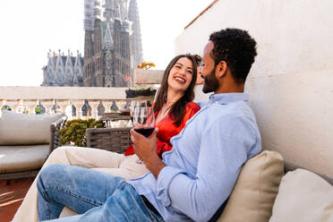 Multiracial beautiful happy couple of lovers dating on rooftop balcony at Sagrada Familia, Barcelona - Multiethnic people having romantic aperitif on a terrace with city view , concepts about tourism and people lifestyle - DMDF08767