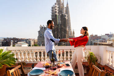 Multiracial beautiful happy couple of lovers dating on rooftop balcony at Sagrada Familia, Barcelona - Multiethnic people having romantic aperitif dinner on a terrace with city view , concepts about tourism and people lifestyle - DMDF08784