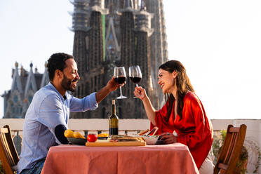 Multiracial beautiful happy couple of lovers dating on rooftop balcony at Sagrada Familia, Barcelona - Multiethnic people having romantic aperitif dinner on a terrace with city view , concepts about tourism and people lifestyle - DMDF08792