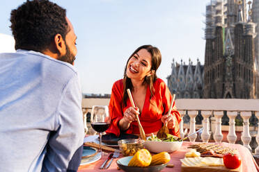 Multiracial beautiful happy couple of lovers dating on rooftop balcony at Sagrada Familia, Barcelona - Multiethnic people having romantic aperitif dinner on a terrace with city view , concepts about tourism and people lifestyle - DMDF08810