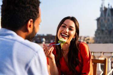 Multiracial beautiful happy couple of lovers dating on rooftop balcony at Sagrada Familia, Barcelona - Multiethnic people having romantic aperitif dinner on a terrace with city view , concepts about tourism and people lifestyle - DMDF08816