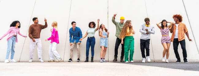 Fröhliche, verspielte, multiethnische Gruppe junger Freunde, die sich im Freien treffen - Multirassische Millennial-Studenten, die sich in der Stadt treffen, Konzepte von Jugend, Lebensstil, Vielfalt, Teenager- und Stadtleben - DMDF08930