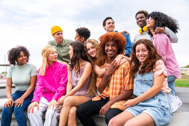 Fröhliche, verspielte, multiethnische Gruppe junger Freunde, die sich im Freien treffen - Multirassische Millennial-Studenten, die sich in der Stadt treffen, Konzepte von Jugend, Lebensstil, Vielfalt, Teenager- und Stadtleben - DMDF08948