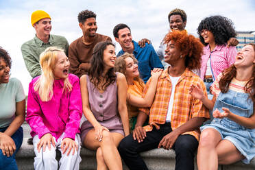 Fröhliche, verspielte, multiethnische Gruppe junger Freunde, die sich im Freien treffen - Multirassische Millennial-Studenten, die sich in der Stadt treffen, Konzepte von Jugend, Lebensstil, Vielfalt, Teenager- und Stadtleben - DMDF08950