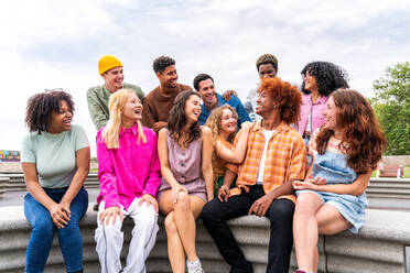 Fröhliche, verspielte, multiethnische Gruppe junger Freunde, die sich im Freien treffen - Multirassische Millennial-Studenten, die sich in der Stadt treffen, Konzepte von Jugend, Lebensstil, Vielfalt, Teenager- und Stadtleben - DMDF08951