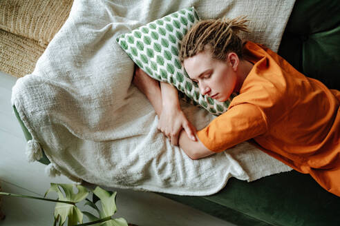 Top view of Young woman sleeping on comfortable sofa with cushion at home near plant in cozy living room of modern apartment - ADSF51039