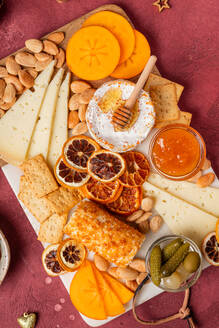 An appetizing cheese platter featuring a variety of cheeses, almonds, honeycomb, crisp crackers, sliced persimmon, and dried citrus, perfect for entertaining. - ADSF51049