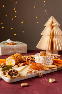 A gourmet selection of cheeses accompanied by honey, crackers, and dried fruits, set against a backdrop of twinkling lights and a paper Christmas tree. - ADSF51050