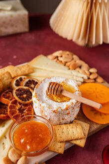 A sumptuous cheese board featuring a selection of fine cheeses, crackers, almonds, dried citrus slices, and a bowl of honey with a dipper. - ADSF51051