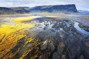 An aerial shot captures the breathtaking river basin in Iceland, set against the dramatic backdrop of rugged cliffs and vibrant, golden terrain - ADSF51071