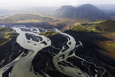 An aerial shot captures the majestic beauty of a meandering river flowing through the volcanic landscapes of Iceland, with mountains in the background - ADSF51086