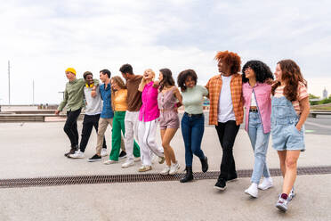 Happy playful multiethnic group of young friends bonding outdoors - Multiracial millennials students meeting in the city, concepts of youth, people lifestyle, diversity, teenage and urban life - DMDF09051