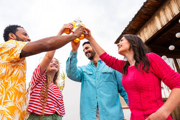 Multiethnic group of happy young friends having dinner barbecue party on rooftop at home - Multiracial cheerful young adult people having fun and bonding on a terrace balcony with city view, eating and drinking. - DMDF09167