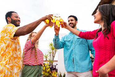 Multiethnic group of happy young friends having dinner barbecue party on rooftop at home - Multiracial cheerful young adult people having fun and bonding on a terrace balcony with city view, eating and drinking. - DMDF09168