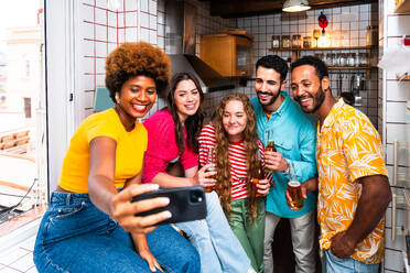 Multiethnic group of happy young friends having dinner barbecue party on rooftop at home - Multiracial cheerful young adult people having fun and bonding on a terrace balcony with city view, eating and drinking. - DMDF09176