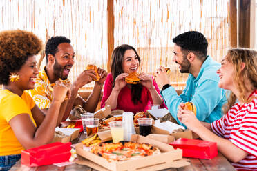 Multiethnic group of happy young friends having dinner barbecue party on rooftop at home - Multiracial cheerful young adult people having fun and bonding on a terrace balcony with city view, eating and drinking. - DMDF09186