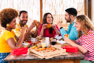 Multiethnic group of happy young friends having dinner barbecue party on rooftop at home - Multiracial cheerful young adult people having fun and bonding on a terrace balcony with city view, eating and drinking. - DMDF09187