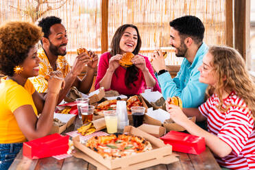 Multiethnic group of happy young friends having dinner barbecue party on rooftop at home - Multiracial cheerful young adult people having fun and bonding on a terrace balcony with city view, eating and drinking. - DMDF09188