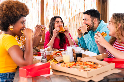 Multiethnic group of happy young friends having dinner barbecue party on rooftop at home - Multiracial cheerful young adult people having fun and bonding on a terrace balcony with city view, eating and drinking. - DMDF09191